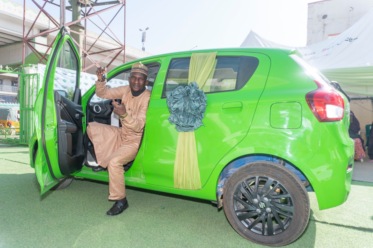 A man sitting in the front seat of a lemon car with a leg out of the car and the door open. He is holding the key to the car he won from Globacom Festival of Joy in Kano